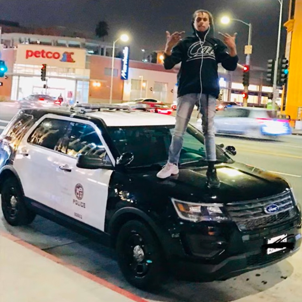 Isaiah Lee, aka rapper Noname Trapper," can be seen on a YouTube photo for his song "David Chappell." He's standing on top of a police car, in jeans, a hoodie, and sneakers that don't match.