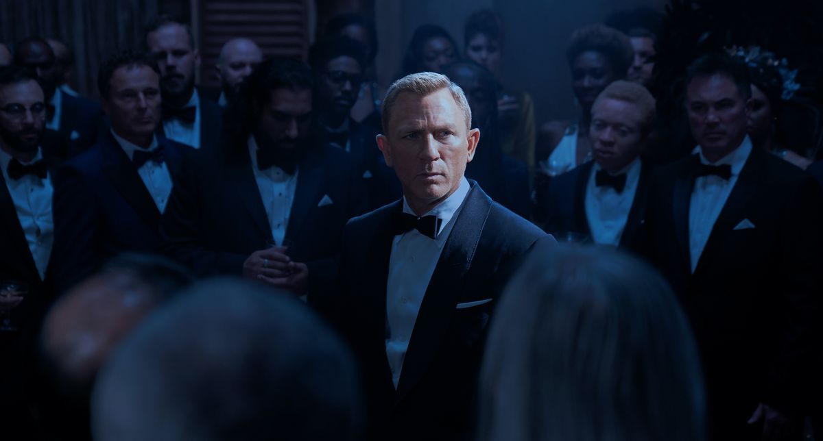 Daniel Craig as James Bond in No Time To Die, in the spotlight surrounded by SPECTER members in formal suits