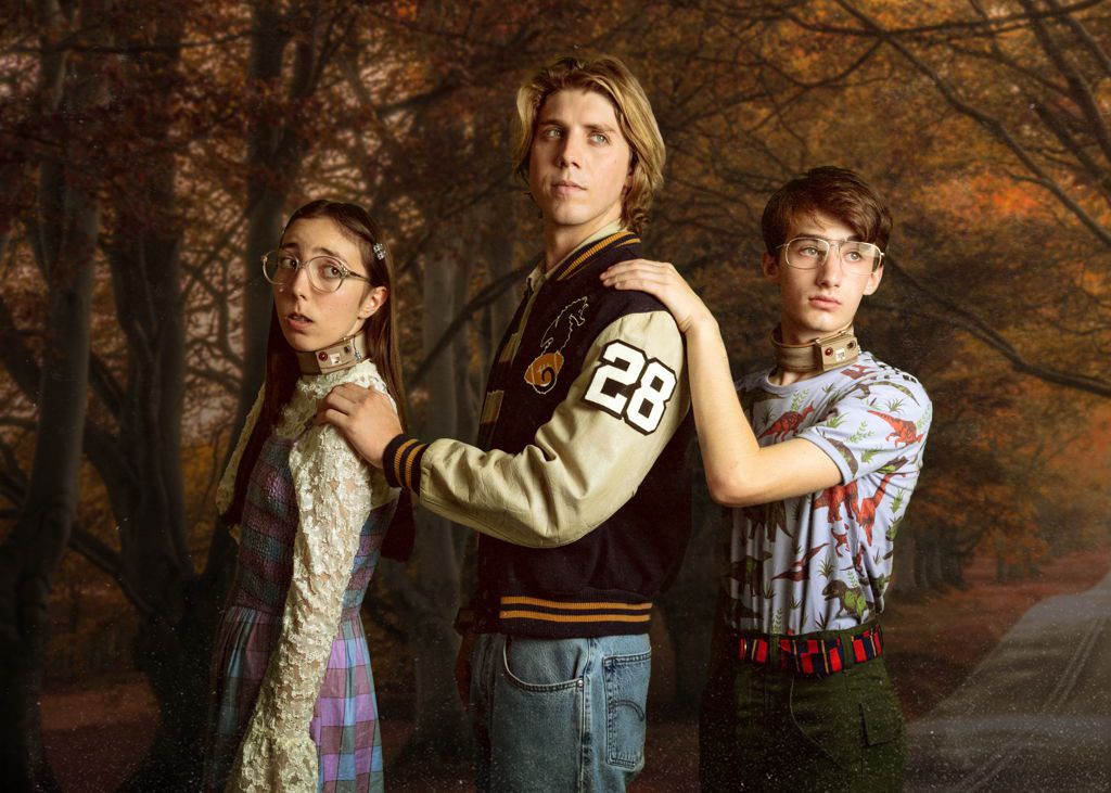 Three teenagers, two with brown electronic collars around their necks, pose for a family portrait in Wyrm.