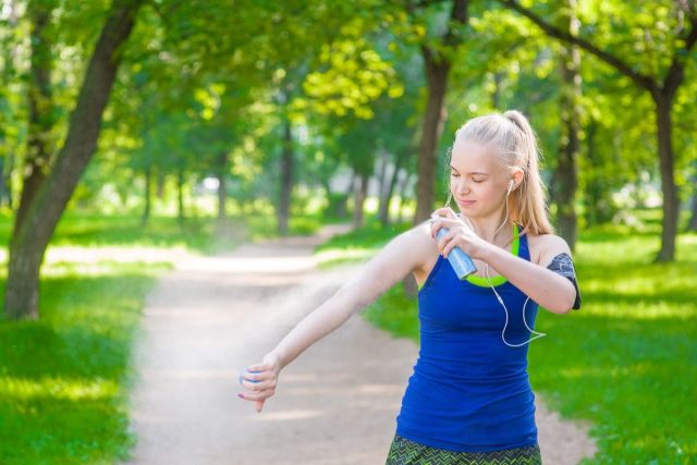 Woman spraying insect repellent on skin before run