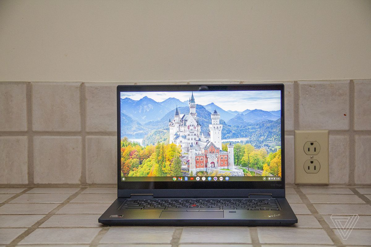 The front of the Lenovo ThinkPad C13 Yoga Chromebook on a tiled counter.  The screen shows a white castle surrounded by trees with mountains in the background.