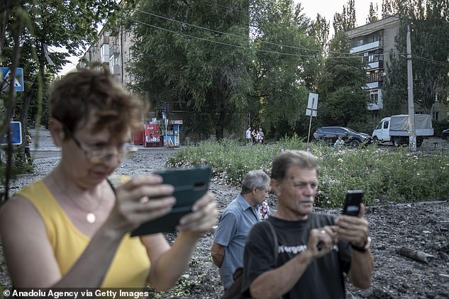 A Bakhmut couple, local Donetsk residents, take photos of a crater left by a Russian missile attack on July 1