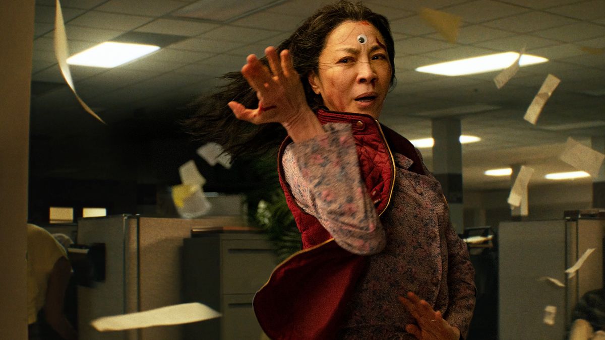 A bloodied Michelle Yeoh with a googly eye on her forehead strikes a martial arts pose in Everything Everywhere All at Once