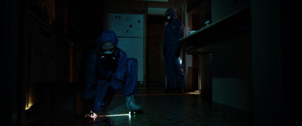 Two figures in hazmat suits inspect the floor of a darkened kitchen during the 11th hour of cleaning.