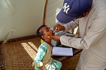 A health worker administers polio vaccine drops to a child in a tent with internally displaced people.