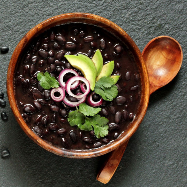 Bowl of black beans garnished with avocado, cilantro, and red onions